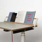 Auf einem Schreibtisch mit einer weißen Holzleiste liegen eine blaue Broschüre, ein schwarzes Tablet und ein aufgeschlagenes Buch, auf dem in roter Schrift „NOW IS A GOOD TIME“ zu lesen ist. Auf der Vorderseite ist das Logo der Smartfurniture GmbH zu sehen, das auf die clevere Schreibtischorganisation hinweist, die vom innovativen Design des „Tiny Top Schreibtischaufsatz White“ inspiriert ist.